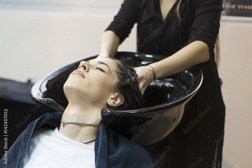 Fototapeta premium Beautiful young woman with hairdresser washing head at hair salon