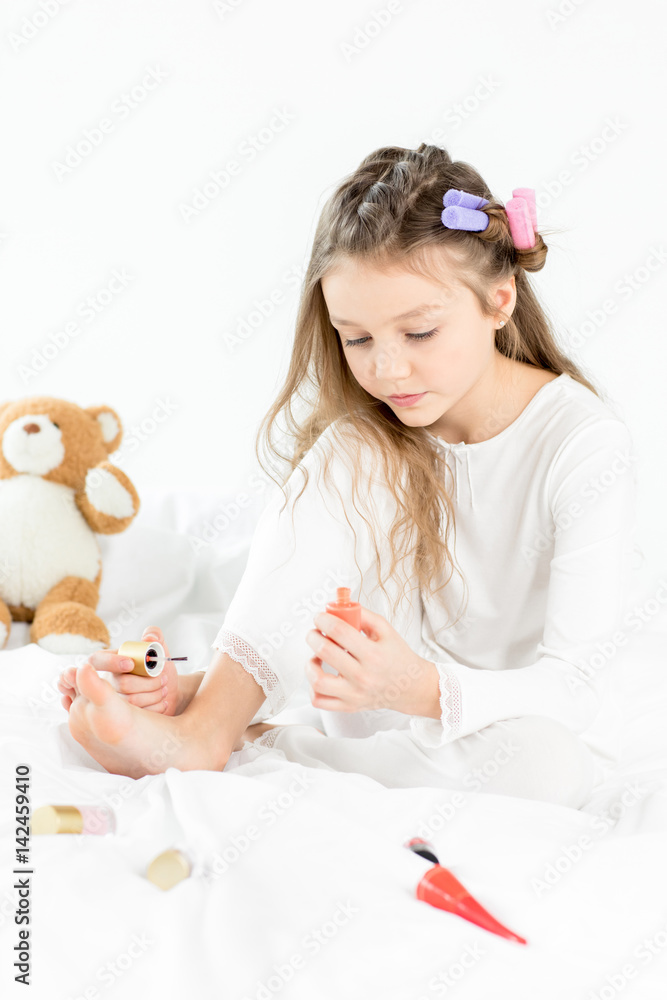 Adorable little girl in pajamas and curlers applying nail polish to toenails Adorable little girl in pajamas and curlers applying nail polish to toenails