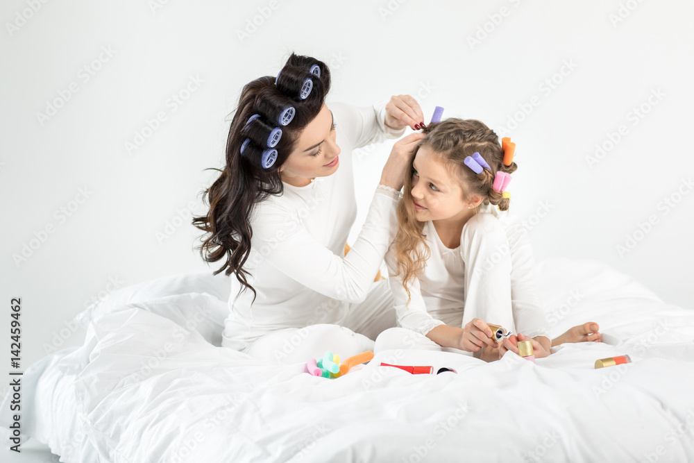 Mother curling hair to daughter applying nail polish on toenails