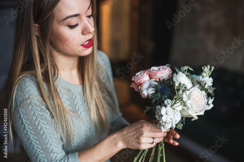 Florist at work: pretty young blond woman holds fashion modern bouquet of different flowersv photo