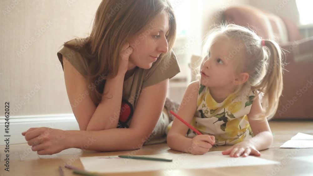 little girl and her mother drawing on the floor at home. On the background of the window. little girl and her mother drawing on the floor at home. On the background of the window.