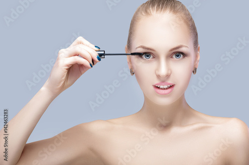beautiful blond woman applying makeup on face on gray background. perfect makeup. brush of mascara 