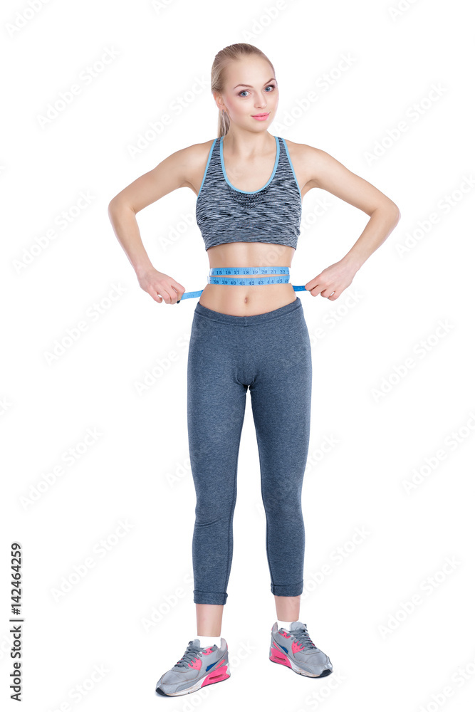 beautiful fitness girl in sportswear measures waist with measuring tape on gray background beautiful fitness girl in sportswear measures waist with measuring tape on gray background