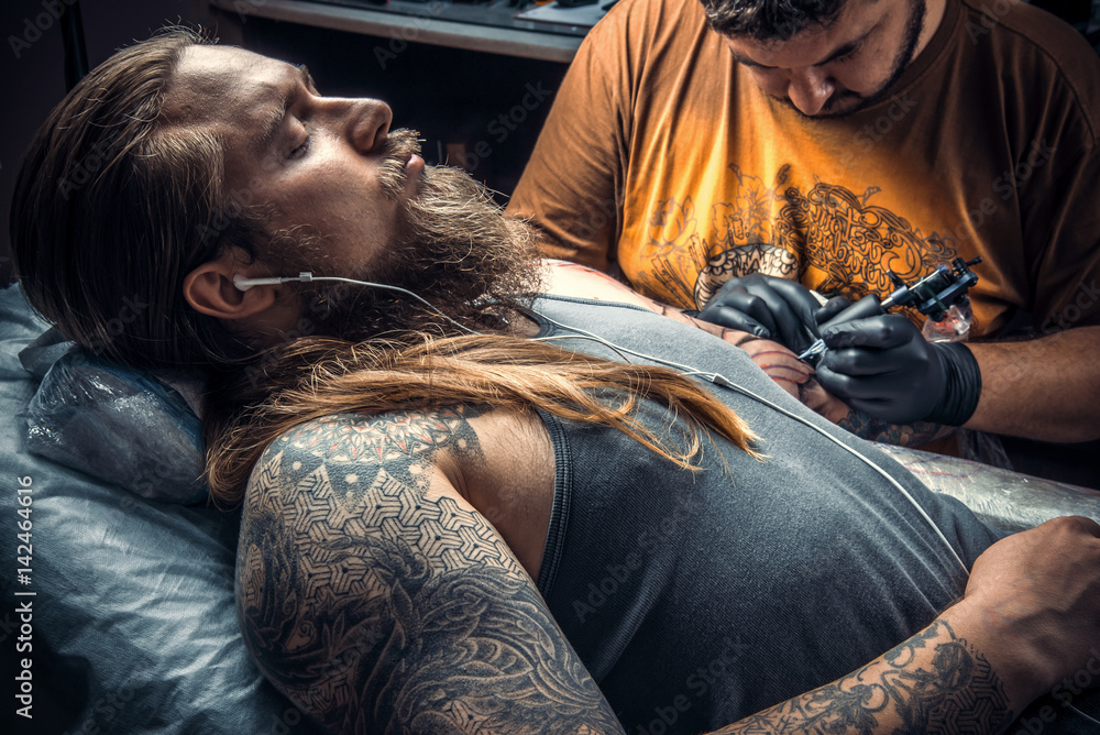Fotografie Tattoo master making a tattoo in tattoo studio