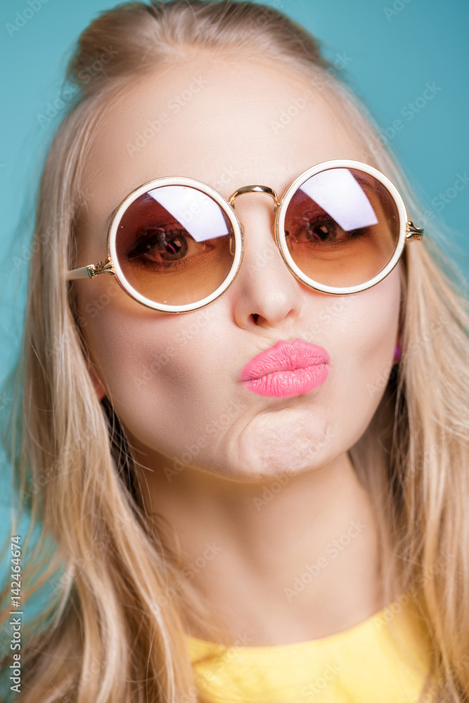 portrait of unhappy and frustrated blond woman in sunglasses and yellow shirt on blue background. portrait of unhappy and frustrated blond woman in sunglasses and yellow shirt on blue background.