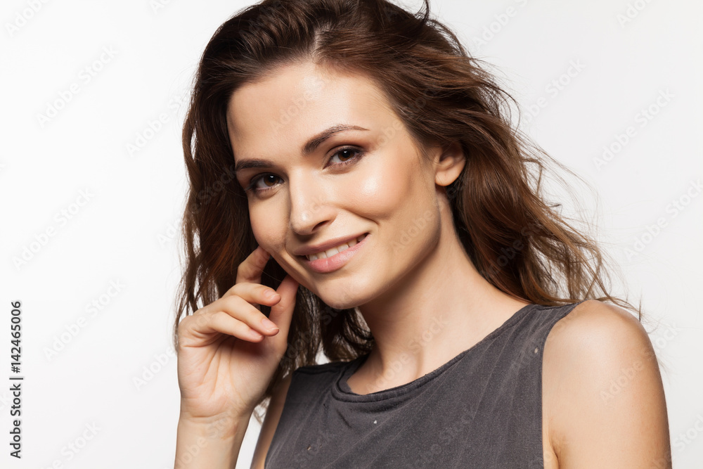 Close-up portrait of smiling young woman with hand near face, in gray dress on white background Close-up portrait of smiling young woman with hand near face, in gray dress on white background
