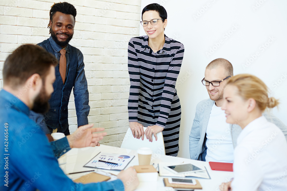 Fototapeta premium Group of creative designers looking at their bearded colleague with interest while he presenting them his ideas concerning joint project in modern boardroom