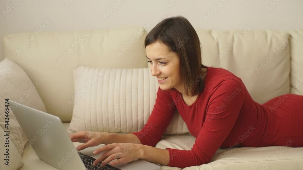 Attractive elegant woman lying down on hotel room sofa and working on laptop. Attractive elegant woman lying down on hotel room sofa and working on laptop.