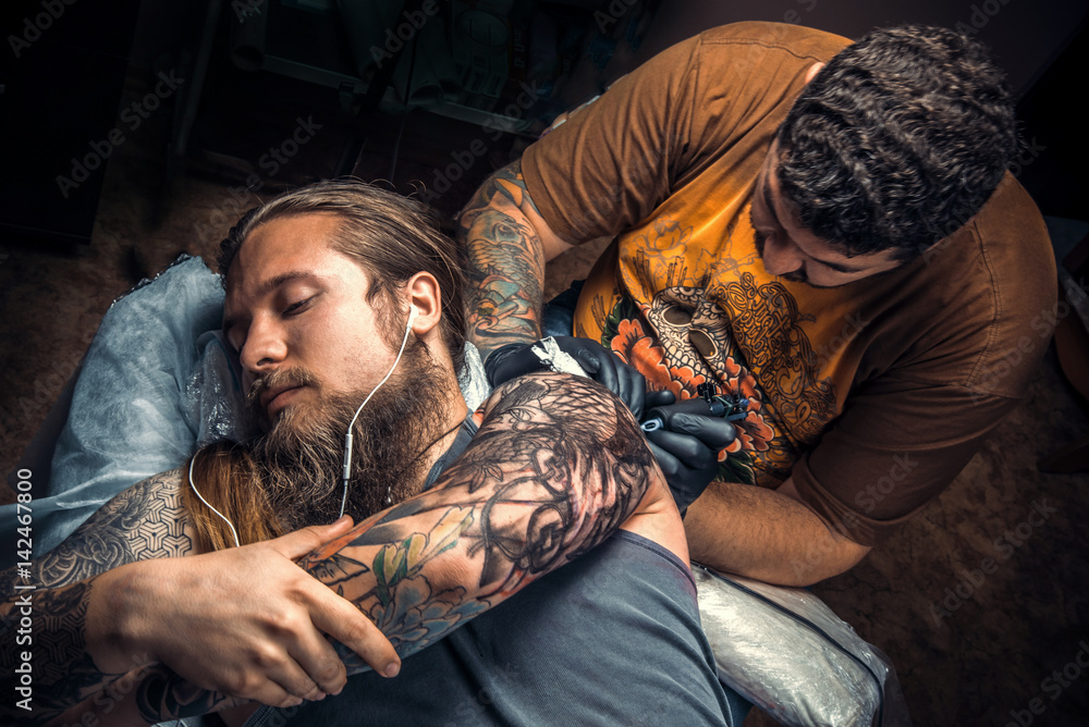 Fototapeta premium Tattoo specialist showing process of making a tattoo in tattoo parlor