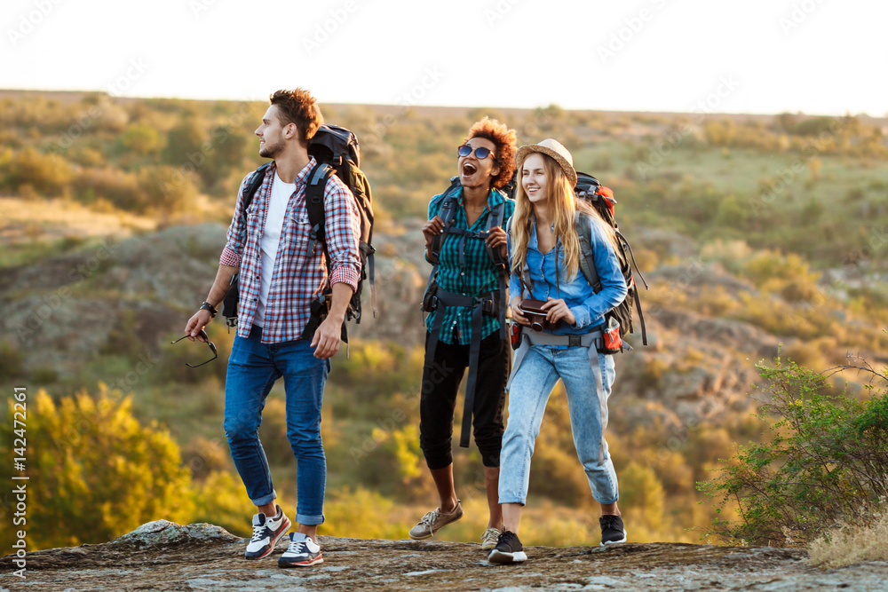 Young cheerful travelers with backpacks smiling, walking in canyon.