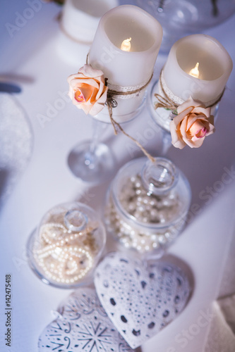 Romantic still life. Burning candles entwined rose flowers, bead, heart. View from above