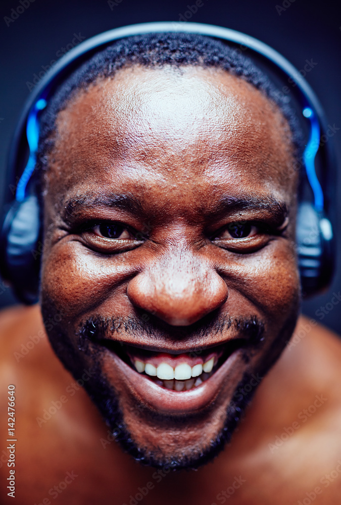 Portrait of cheerful African American music lover in headphones wrinkling nose and smiling from ear to ear while looking at camera Portrait of cheerful African American music lover in headphones wrinkling nose and smiling from ear to ear while looking at camera