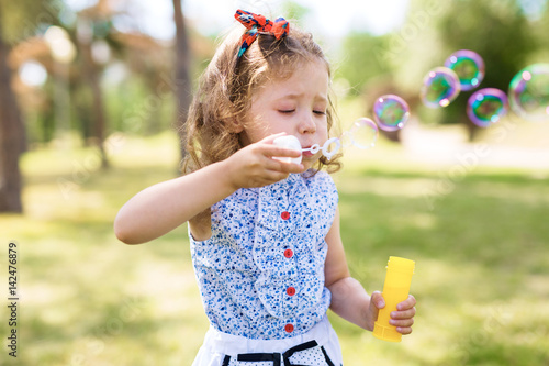 Cute little girl with headband blowing soap bubbles on a summer day in park