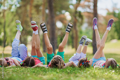 Children lying on green grass in park on a summer day with their legs lifted up to the sky