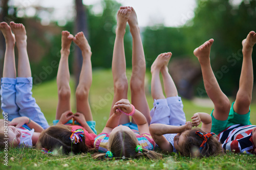 Kids lying on green grass barefoot and enjoying summer day with legs lifted up to the sky photo