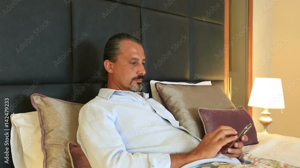 middle age brunette man using smartphone lying on bed at home middle age brunette man using smartphone lying on bed at home