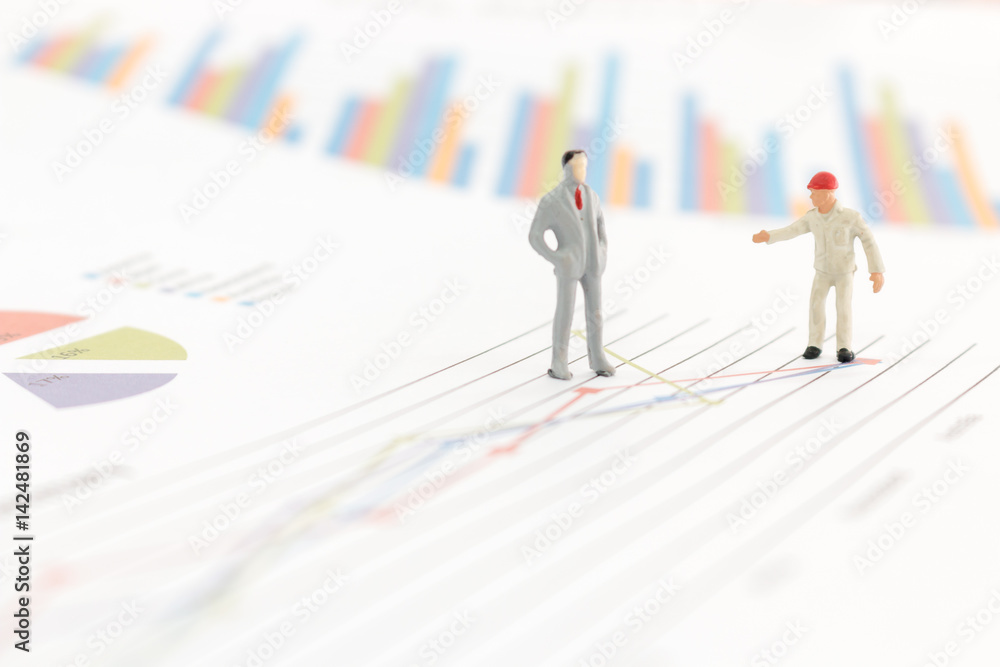 Miniature figures businessman standing on a graph chart Miniature figures businessman standing on a graph chart