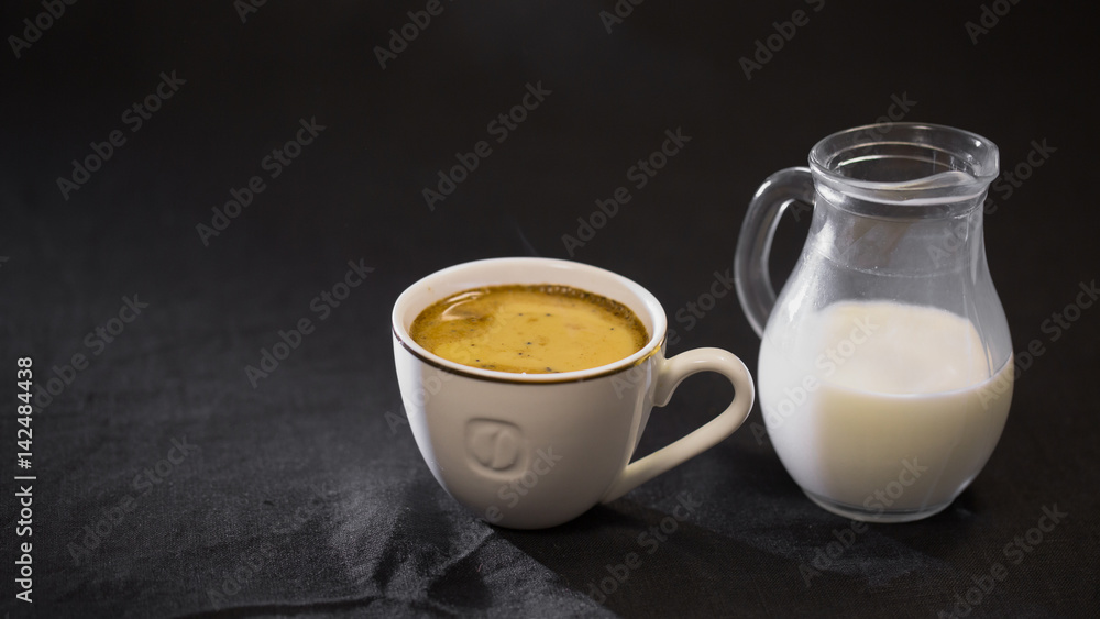 coffee in a white Cup milk in a small jug on black background. coffee in a white Cup milk in a small jug on black background.