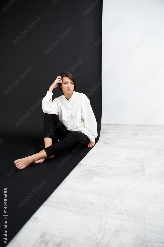 Young beautiful girl sitting on floor over black and white background. Young beautiful girl sitting on floor over black and white background.