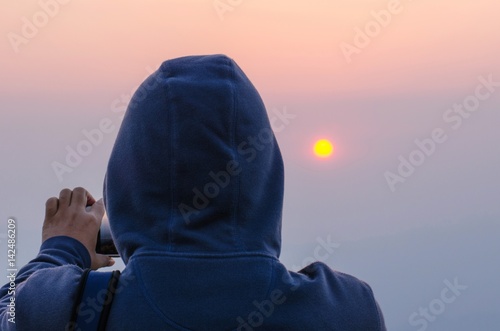 hipster traveler holding smart phone taking photo of beautiful sunset at mountain,with grain, image contain certain grain or noise and soft focus, color tone effect.