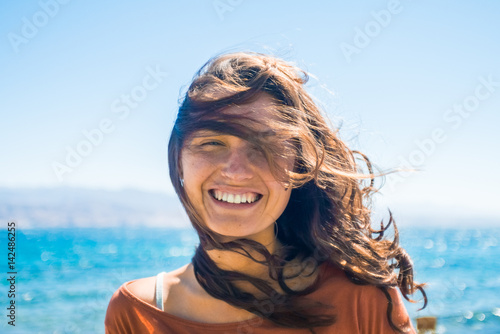 Portrait of happy smiling young woman on beach and sea background. Wind plays with girl long hair © justfreez