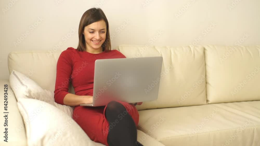 Beautiful woman with short hair sitting on sofa in the room and smiling using the laptop Beautiful woman with short hair sitting on sofa in the room and smiling using the laptop