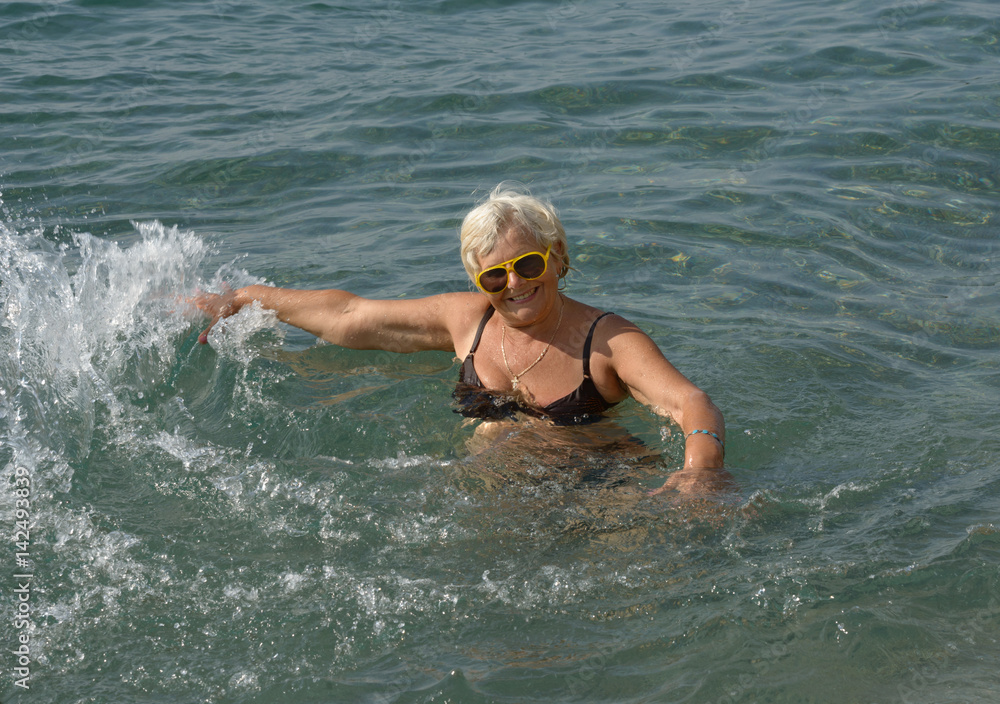 Aged woman is doing motions in clear sea water.