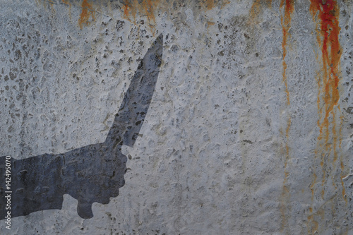 Human hand with knife silhouette in shadow on concrete wall and blood background, with space for text or image.