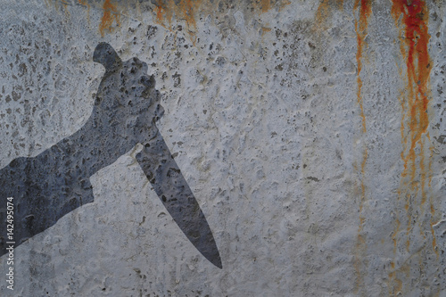 Human hand with killing knife silhouette in shadow on concrete wall and blood background, with space for text or image.