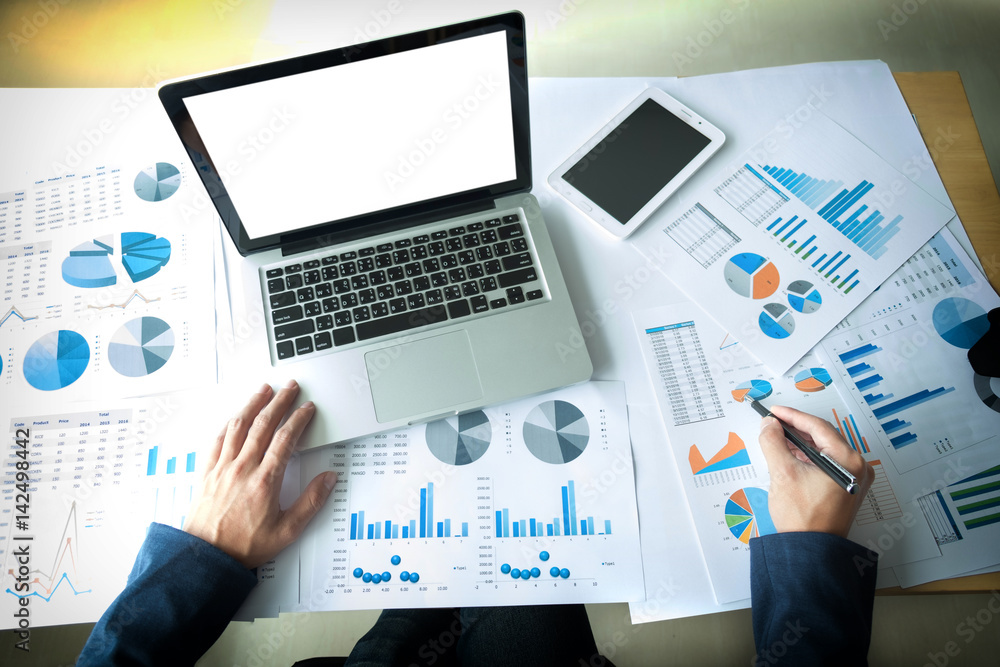 Business man working at office with laptop, tablet and graph data documents on his desk, top view Business man working at office with laptop, tablet and graph data documents on his desk, top view
