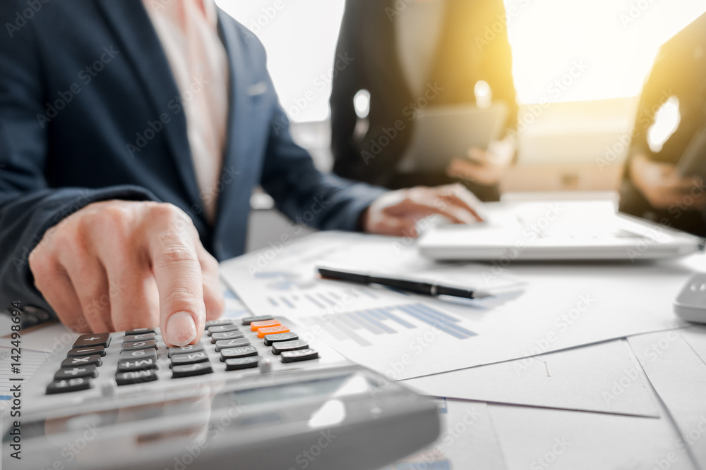 Business team using a calculator to calculate the numbers on his desk in a office. Business team using a calculator to calculate the numbers on his desk in a office.