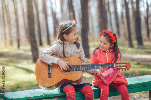 Two little sisters singing and playing the guitar sitting on the bench photo