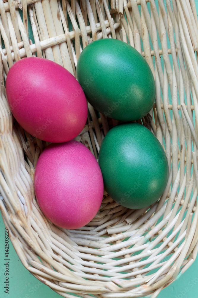 four colored easter eggs in basket on green background