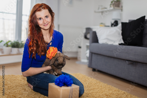 Smiling woman sitting on the floor holding bunny as a gift.