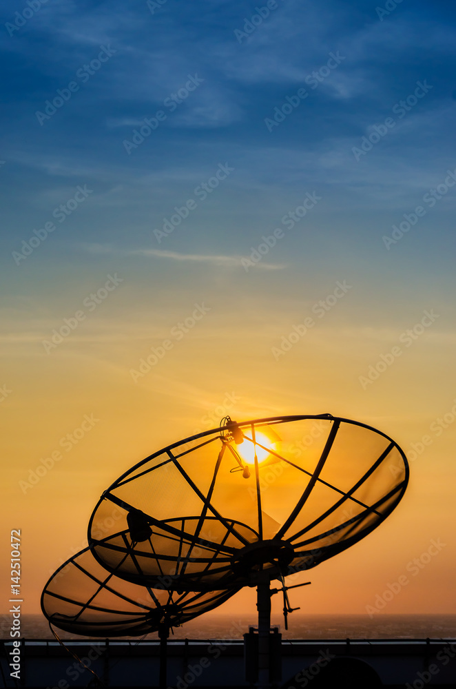 Satellite dish communication technology network silhouette (black shadow) on building rooftop with yellow gold sunset and blue sky background in urban or city area