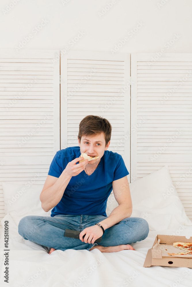 Man watching TV sitting on the bed and eating pizza Man watching TV sitting on the bed and eating pizza