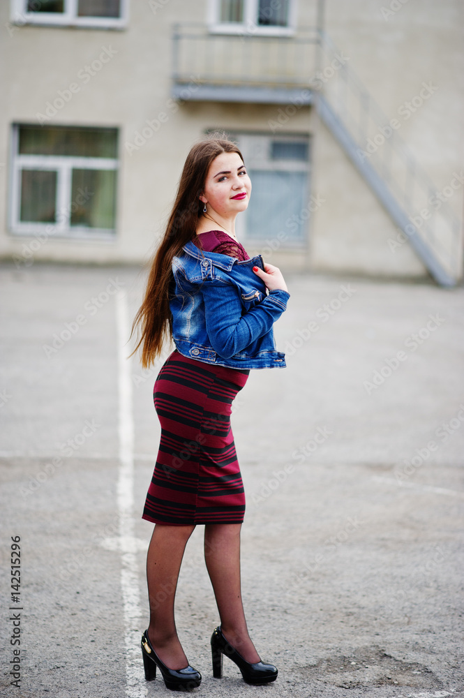 Young chubby teenage girl wear on red dress and jeans jacket posed against school backyard.