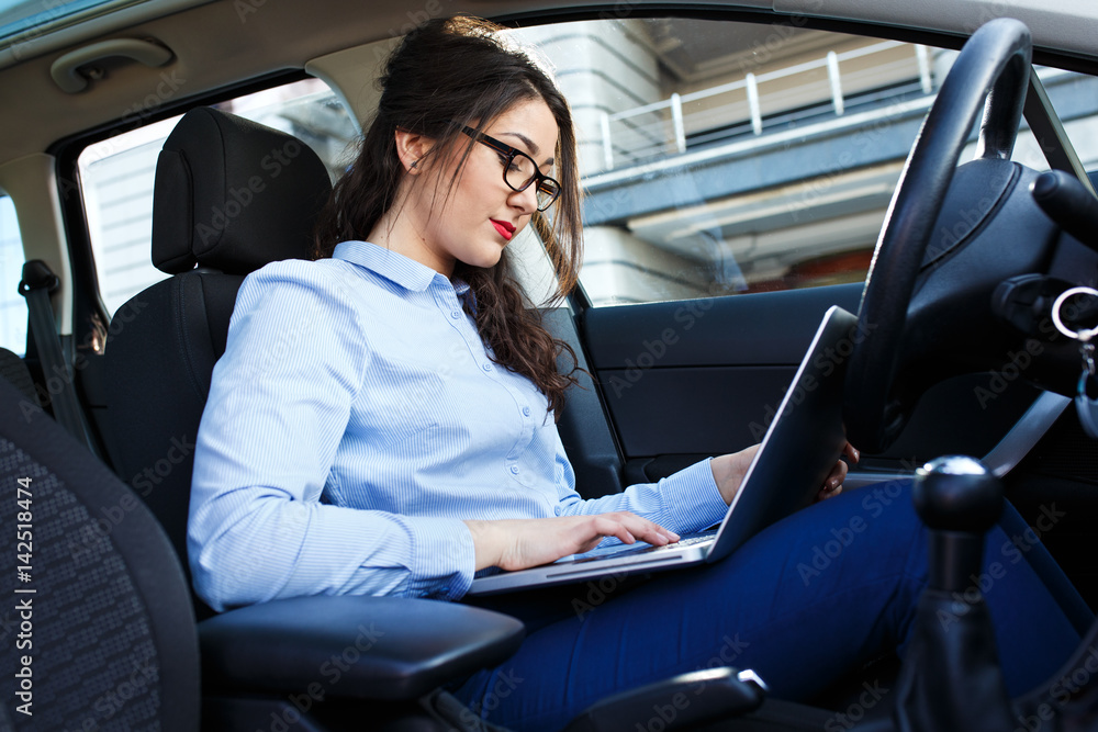 Beautiful young business woman using laptop and phone in the car.
