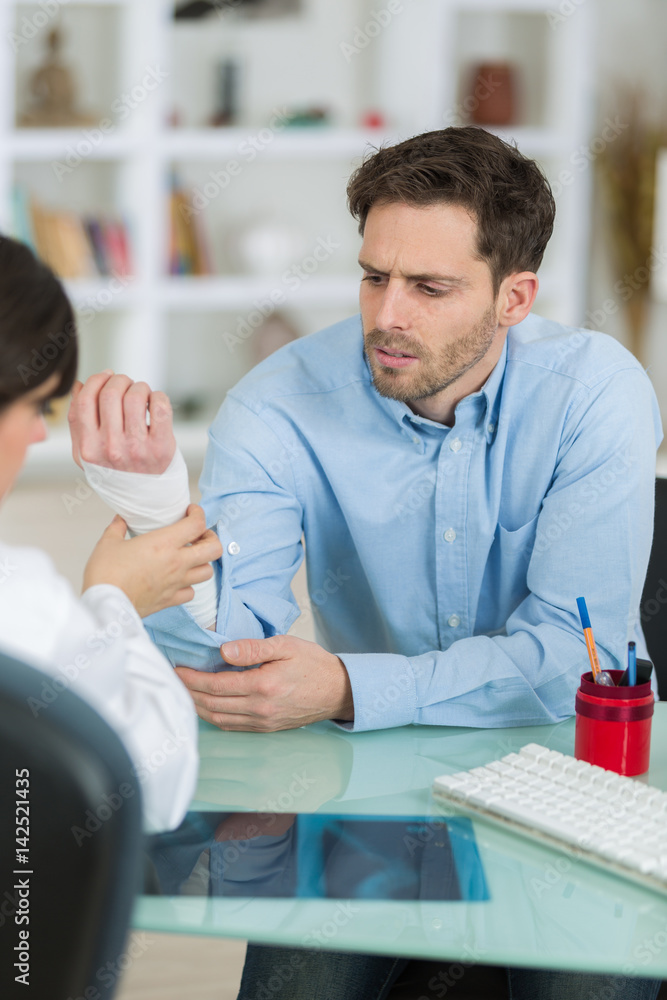 young attractive female doctor bandaging hand of male patient young attractive female doctor bandaging hand of male patient