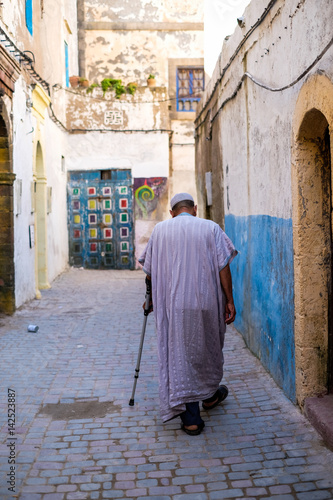 old arabic man with a stick is walking along the street in Morocco