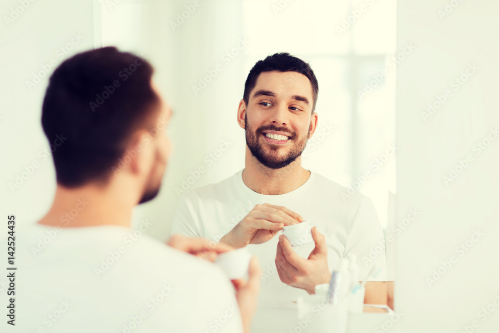 Obraz premium happy young man applying cream to face at bathroom