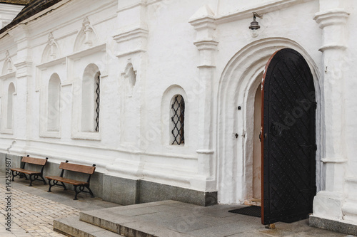 Open medieval door with metal decoration in white wall of old orthodox church.