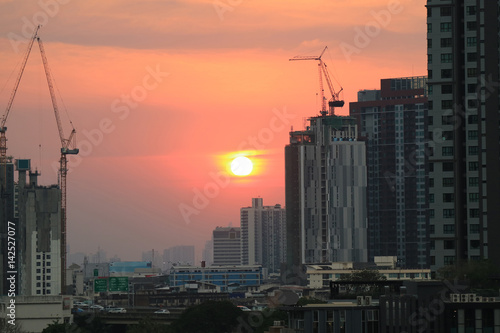 Sun setting on pastel orange sky amongst working cranes of the construction site  Bangkok  Thailand 