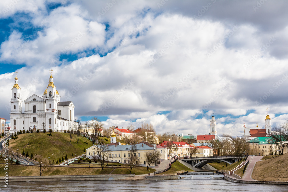 City architecture, on the bank of the river there is a Christian church, a monastery of the princess, a chapel / town hall, a small bridge connects two banks, footpaths, a sunny day, Belarus Vitebsk