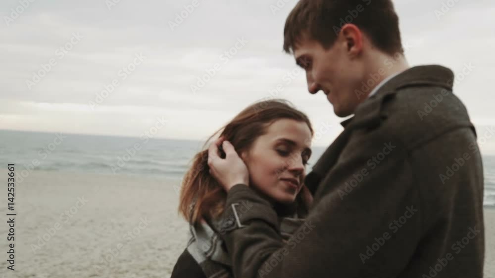 Young couple looking at the sea, walking the beach, coat and hat, Baltic or Iceland cold weather close-up shot Young couple looking at the sea, walking the beach, coat and hat, Baltic or Iceland cold weather close-up shot