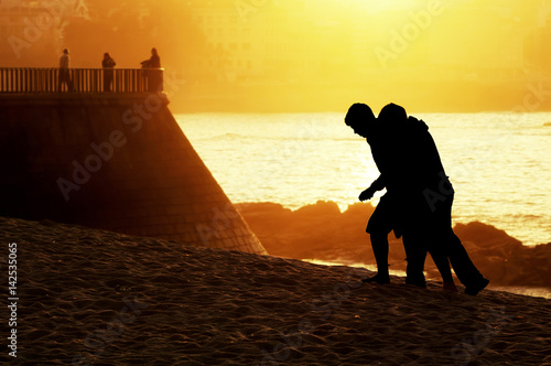 Friends walking on the beach at sunset, unrecognizable silhouettes
