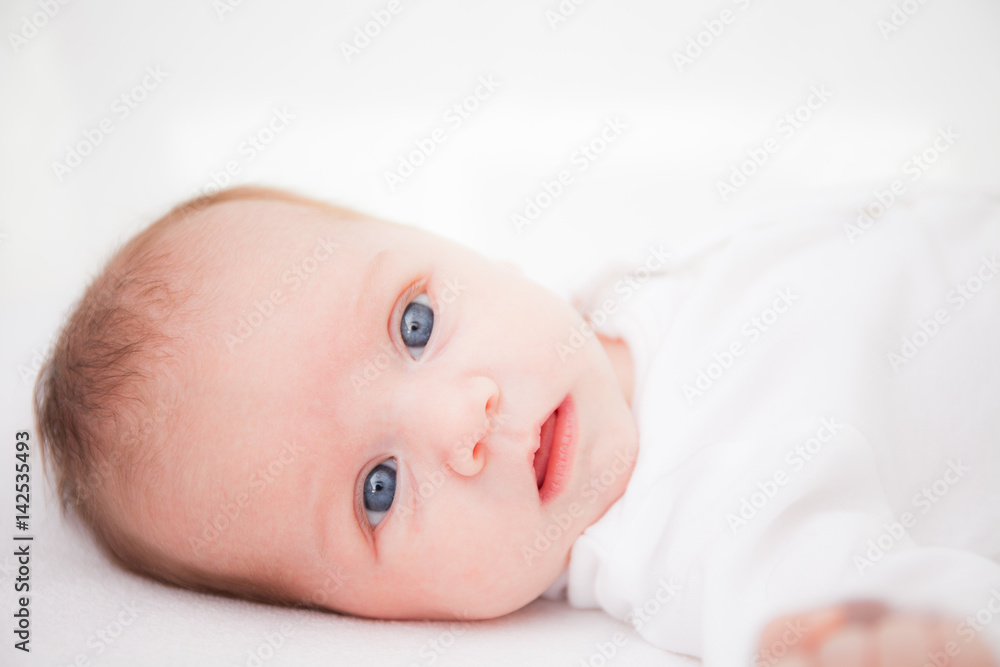 Cute adorable newborn baby girl in white bed and looking at the camera