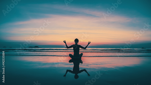 Sunset yoga woman meditation on sea coast with reflection in water.