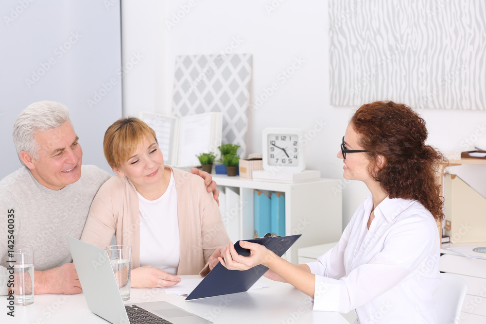 Middle aged couple discussing terms of insurance contract with agent sitting at table in office Middle aged couple discussing terms of insurance contract with agent sitting at table in office