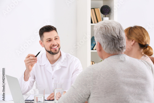 Middle aged couple discussing terms of insurance contract with agent sitting at table in office